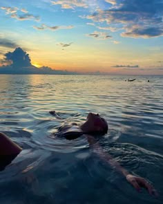 a person floating in the ocean at sunset with their head above the water's surface