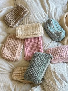 five knitted mittens laid out on a bed with white sheets and one is pink, the other blue