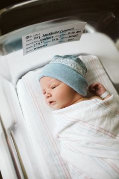 a baby in a crib is wearing a blue hat and has a name tag on it