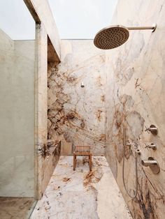 a bathroom with marble walls and flooring, shower head and bench in the corner