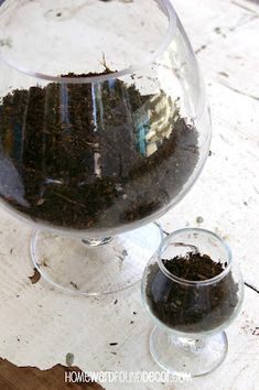 a glass vase filled with dirt sitting on top of a wooden table next to a cup