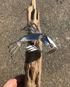 a hand holding a metal bird on top of a piece of wood