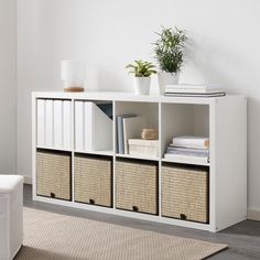 a white shelf with baskets and plants on top in a room next to a couch