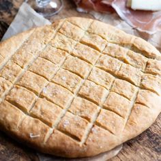 an uncooked bread on a cutting board with cheese and meat in the background