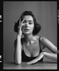 a black and white photo of a woman sitting at a table with her hand on her face