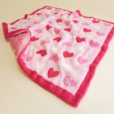 a pink blanket with hearts on it sitting on top of a white table next to a cup