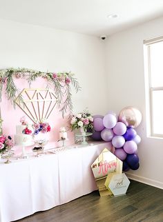 a table topped with balloons and cake next to a window filled with pink, purple and white flowers