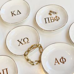 six white plates with gold greek letters on them and a golden chain around the edges