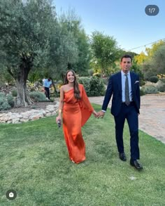 a man and woman in formal wear holding hands walking on grass with trees in the background