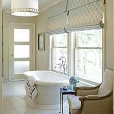 a bath tub sitting next to a window in a bathroom with white walls and tile flooring