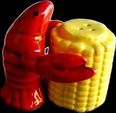 a corn cob shaped like a lobster next to a red and yellow pepper shaker