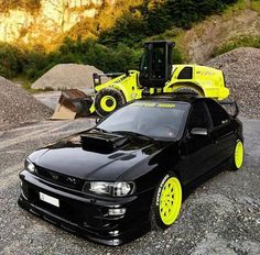 a black car with yellow rims parked next to a bulldozer