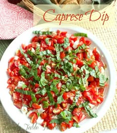 caprese dip with tomatoes and basil in a white bowl on a table next to bread