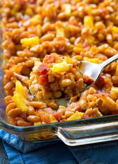 a casserole dish filled with baked beans and pineapple chunks, topped with a spoon