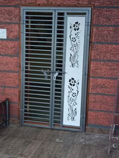 an iron gate with flowers painted on it in front of a red brick wall and bench