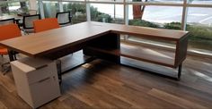 an office desk with orange chairs in front of large windows