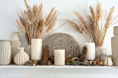 some candles are sitting on a mantel with dried grass and other items around it