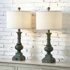 two green lamps sitting on top of a dresser next to a white brick wall in a room