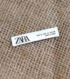 a metal name tag sitting on top of a piece of burlied fabric with the word zara printed on it