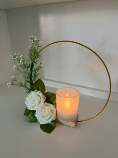 a candle and some flowers on a white table with a gold ring around the center