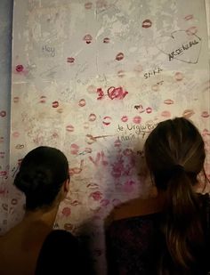 two girls writing on a wall with lipstick