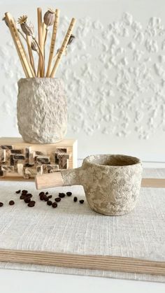 a coffee cup sitting on top of a table next to some wooden sticks and beans