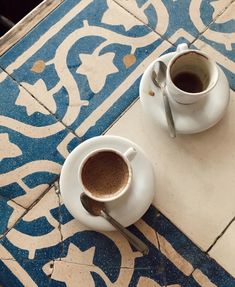 two cups of coffee sitting on top of a blue and white tile floor