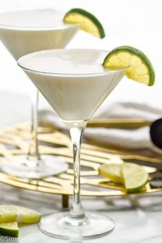 two martini glasses filled with white liquid and lime wedges on a gold serving tray