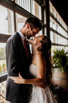 a bride and groom kissing in front of a window