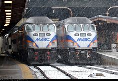 two trains parked next to each other on train tracks in the snow at a station