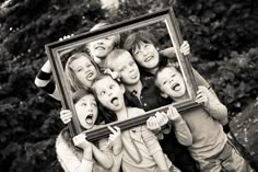 a group of young children holding up a framed photo in front of them with their mouths open