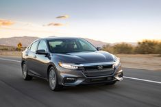 the front end of a gray honda civic hatchback driving down a road with mountains in the background