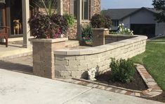 a brick wall in front of a house with flowers and plants growing on the planters