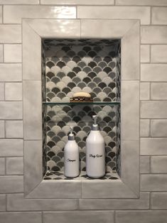 two bottles are sitting on the shelf in front of a tiled niche with soap and lotion