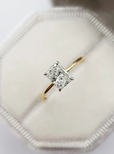 an engagement ring in a box on a white surface, with the diamond set in it's center