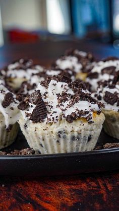 there are many cupcakes with white frosting and chocolate chips on top, sitting on a black plate