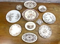 a table topped with lots of plates on top of a wooden table covered in white and brown designs