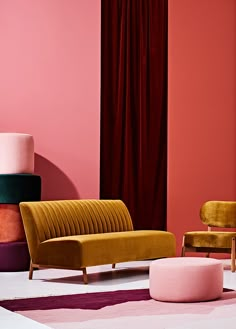 three different colored chairs and one pink ottoman in front of a wall with red curtains