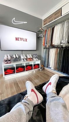 two people laying on the floor in front of a large screen tv with shoes hanging from it