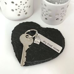 a heart shaped rock with a keychain and two mugs behind it that says my first home