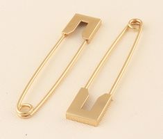 two gold tone metal clips on a white surface with one clip in the shape of a letter