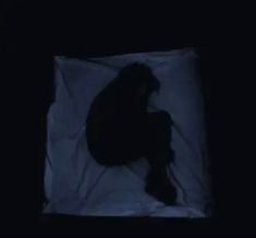 the silhouette of a person sitting on a sheet in the dark