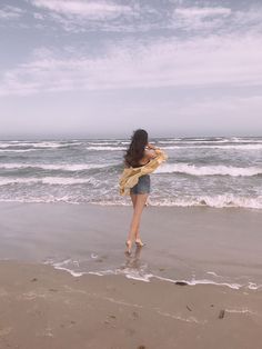 a woman is running on the beach with her scarf around her neck and feet in the water