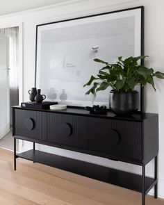 there is a plant on top of the black dresser in this room with white walls