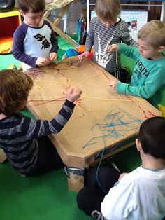 several children are sitting at a table and playing with string art on the cardboard board