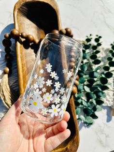 a hand holding a glass with white flowers on it