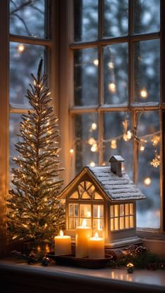 a lit christmas tree in front of a window with a small house next to it