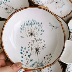 a person holding a plate with blue flowers on it next to other plates and bowls