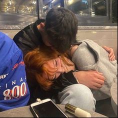 two people sitting on a bench with their heads close to each other and one person covering his face