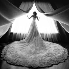 a woman standing in front of a window wearing a wedding dress and holding her arms out